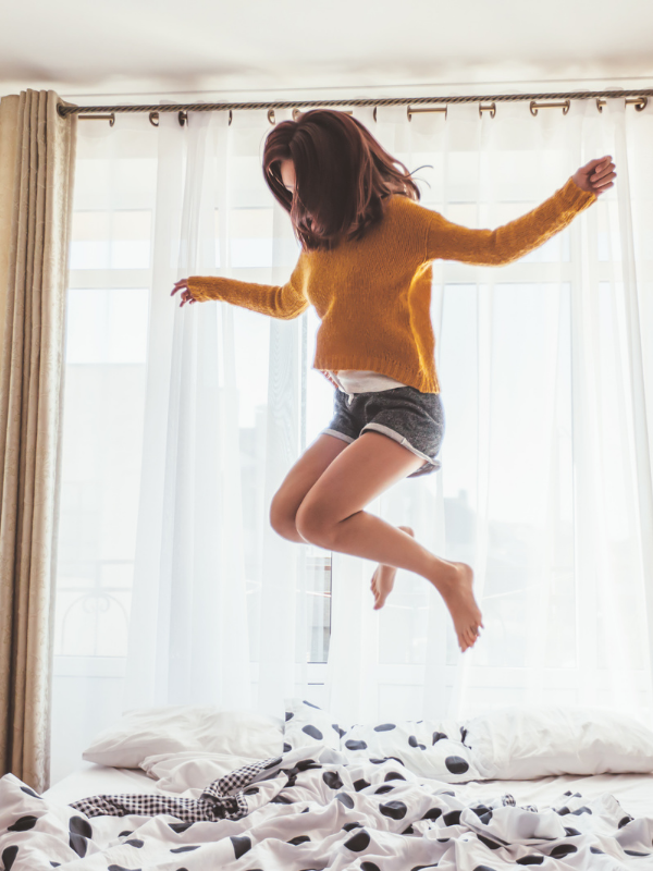woman in her early 20s jumping on the bed