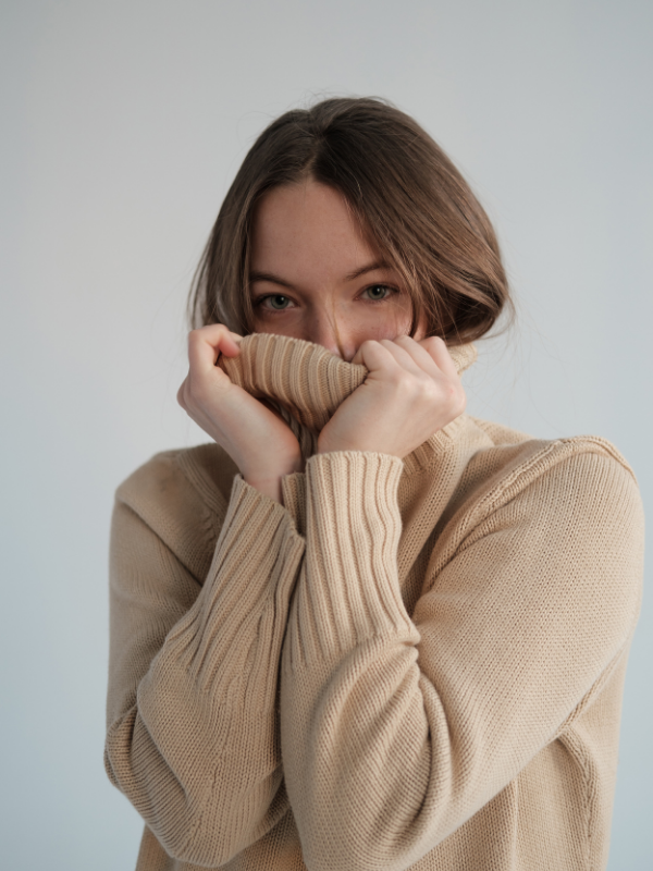 woman with a knitted sweater hiding her face with it