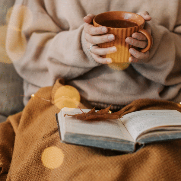 a woman snuggled on the sofa with a blanket, book and a coffee mug