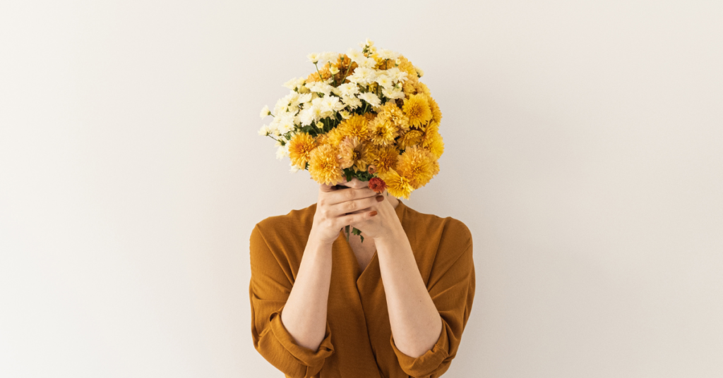 a woman in a brown dress holding a sunflower bouquet in front of her face