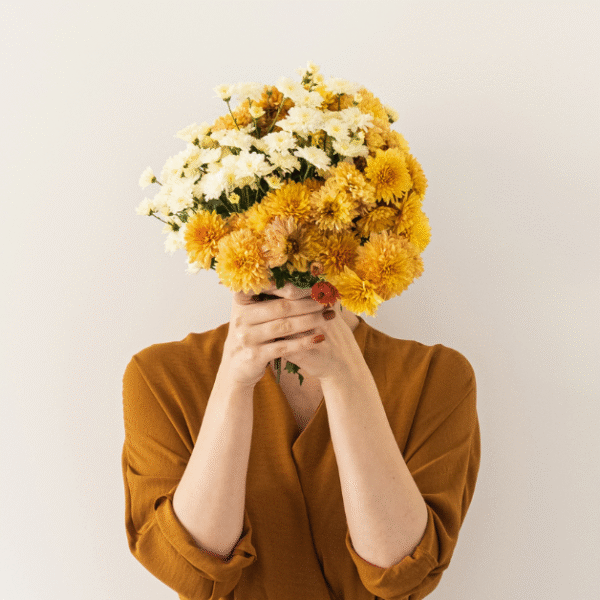 a woman in a brown dress holding a sunflower bouquet in front of her face