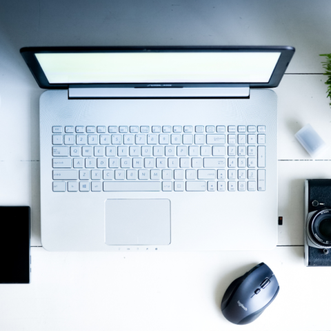 featured image for post on digital declutter and detox showing a desk top and a laptop, phone, camera, plant and headphones flat lay